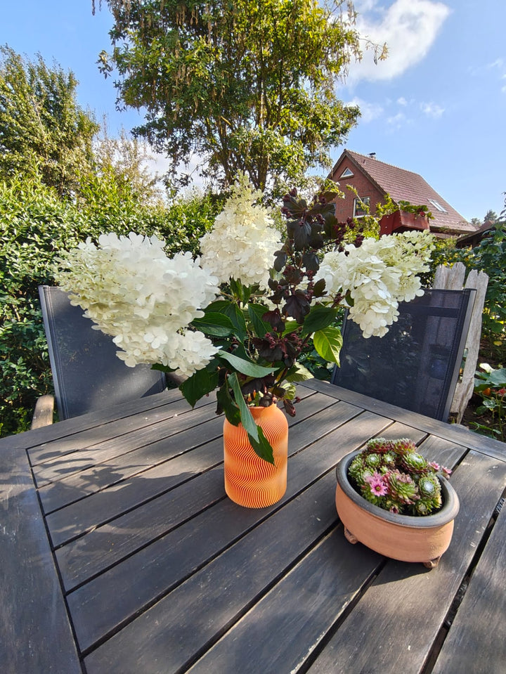 Luna Vase in Orange mit weißen Hortensien auf dem Gartentisch – Kundenfoto